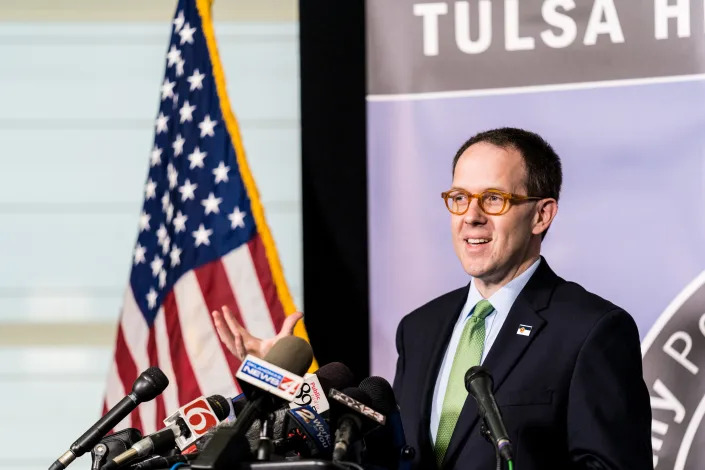 G.T. Bynum, mayor of Tulsa, at the podium in front of a bank of microphones and an American flag.